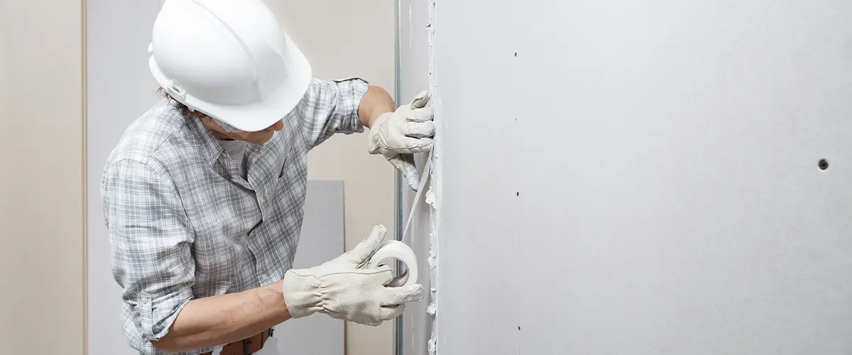 man drywall worker or plasterer putting mesh tape for plasterboard on a wall using a spatula and plaster.