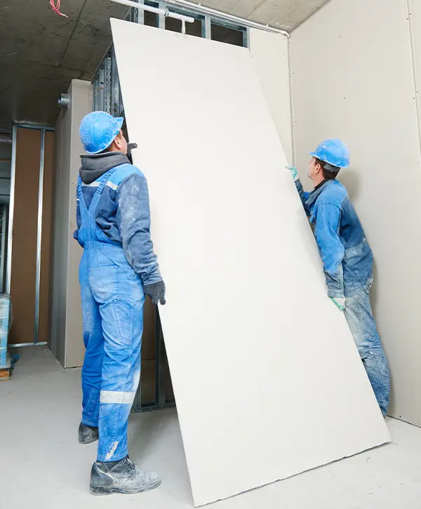 Two men installing a board of drywall on a wall structure.