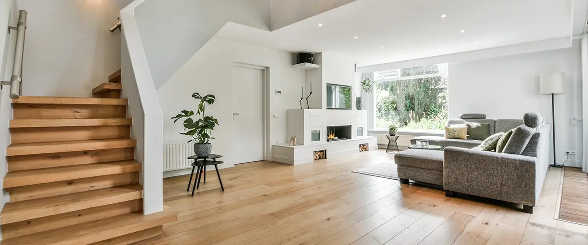 Cozy house interior with a wooden floor, large gray sofa, and stairs leading to the second floor.