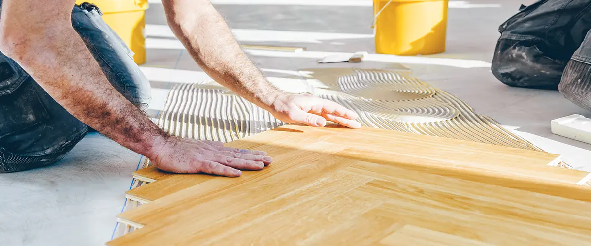 Worker installing wooden parquet flooring in a bright interior space.