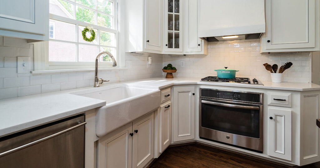 Bright kitchen with white cabinetry, stainless steel appliances, apron sink, and large window over the sink providing natural light
