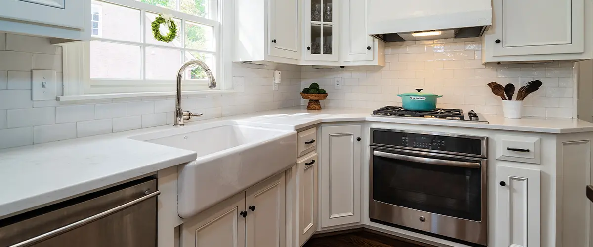 Bright kitchen with white cabinetry, stainless steel appliances, apron sink, and large window over the sink providing natural light