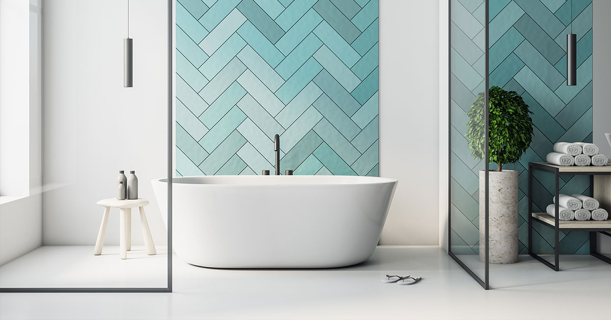Modern bathroom with a freestanding white bathtub against a blue herringbone tile wall, glass partition, and minimalist decor.