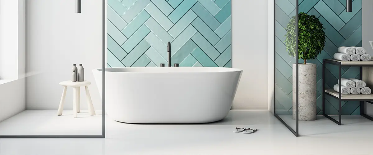 Modern bathroom with a freestanding white bathtub against a blue herringbone tile wall, glass partition, and minimalist decor.