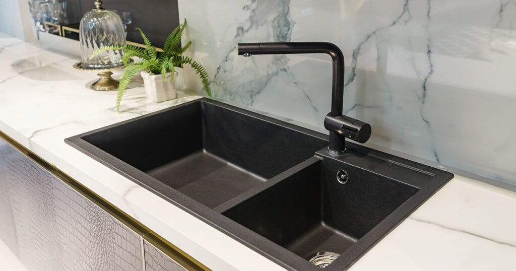 Modern kitchen sink size with black faucet, marble countertop, and backsplash, featuring potted plant and glass cake dome for decor.