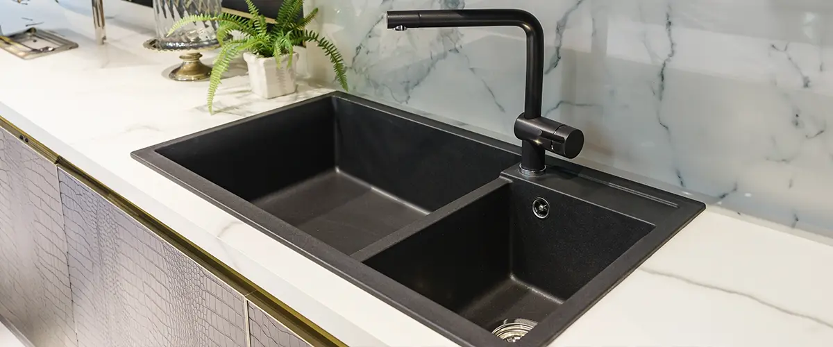 Modern kitchen sink size with black faucet, marble countertop, and backsplash, featuring potted plant and glass cake dome for decor.