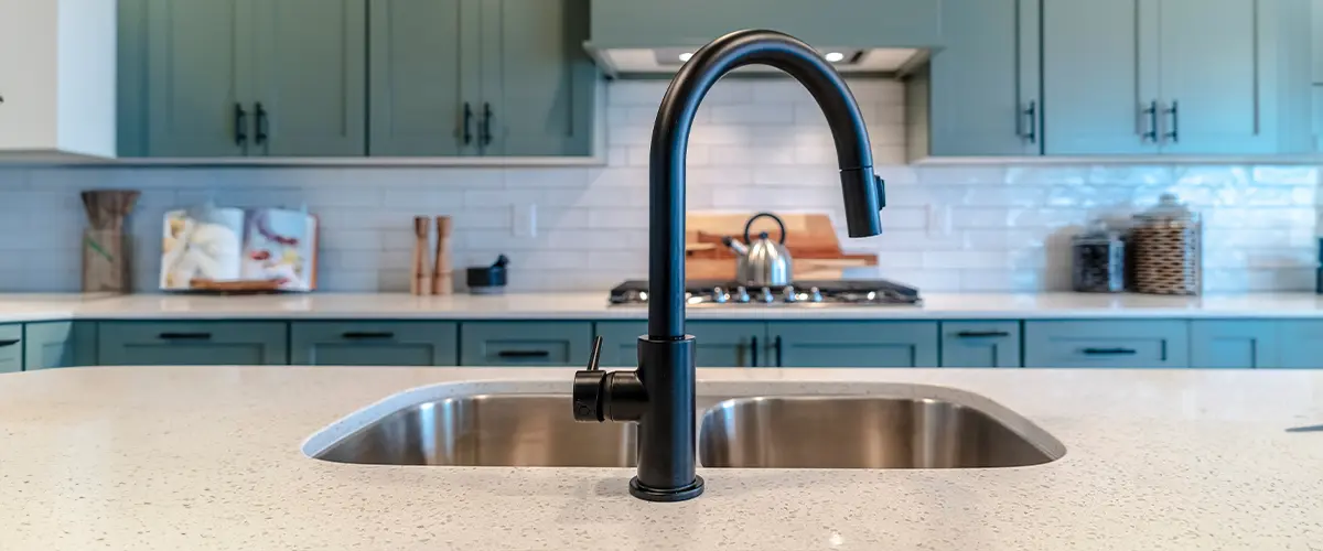 Modern kitchen with black faucet, quartz countertop, stainless steel sink, and sage green cabinets, offering a sleek design.