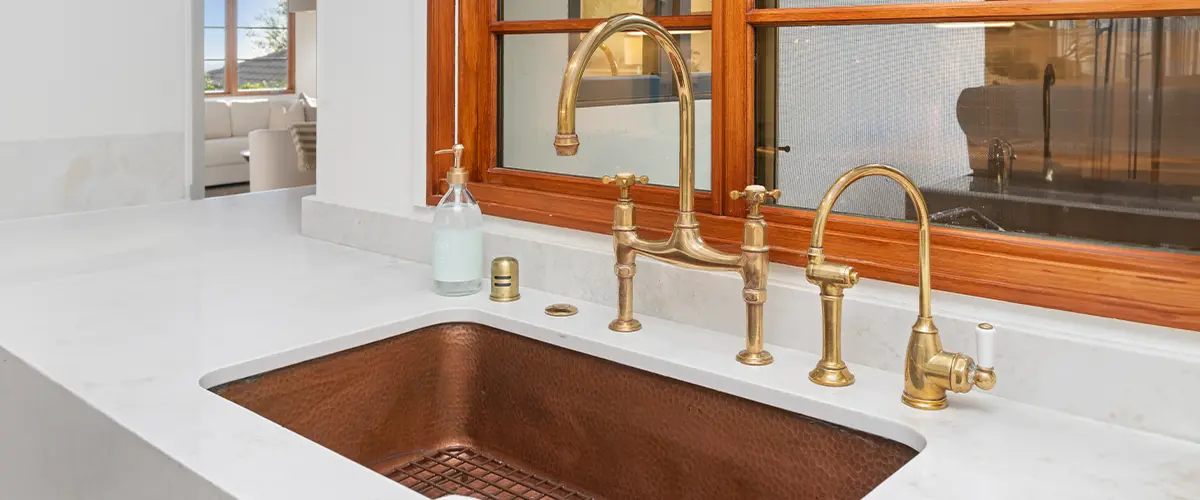 Modern kitchen with elegant brass fixtures and hammered copper sink, featuring a marble countertop and classic tile backsplash.