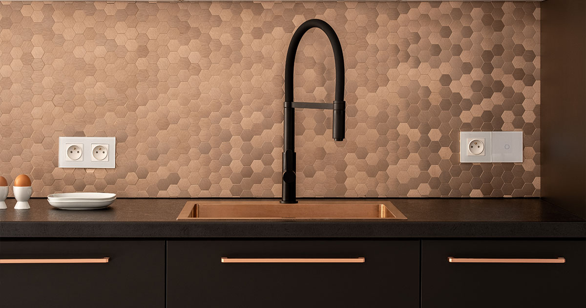 Modern kitchen with matte black cabinets, rose gold handles, a black faucet, and a copper hexagonal tile backsplash
