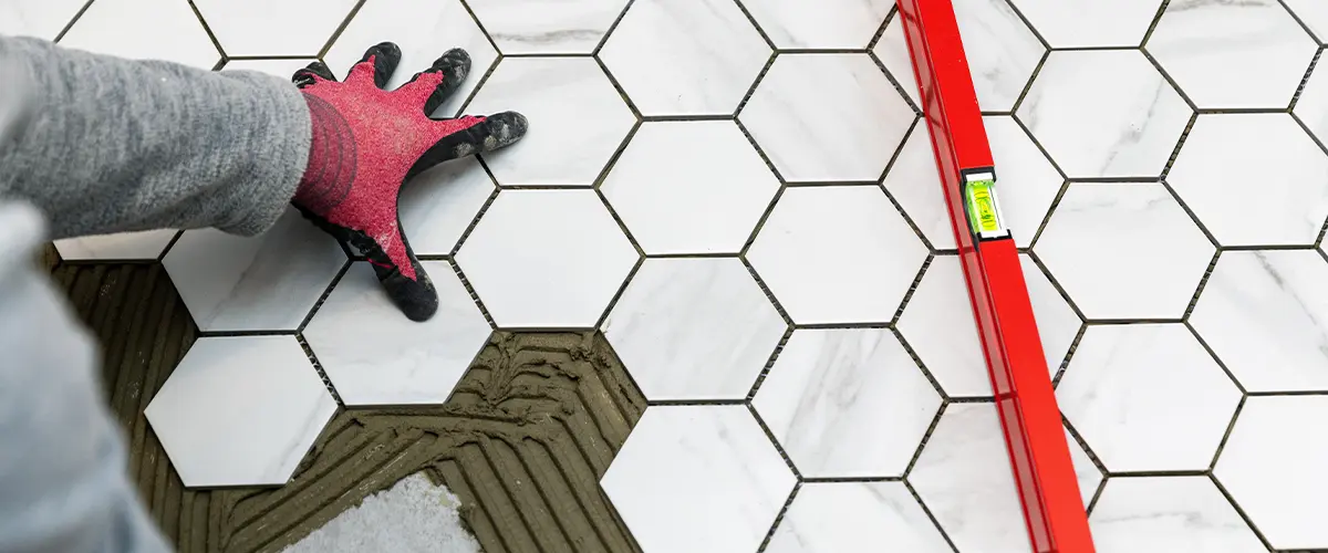 Worker installing hexagonal floor tiles with red level tool, ensuring precision and alignment for a professional finish.