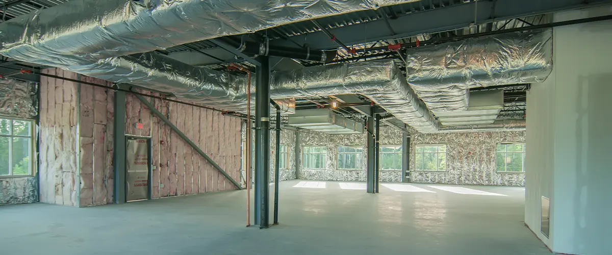 Commercial building interior under remodeling with exposed ductwork, insulation, and large windows.