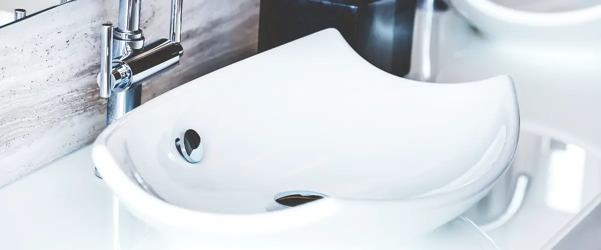 Elegant white vessel sink with a chrome faucet, set against a marble backsplash, with a tissue box in the background