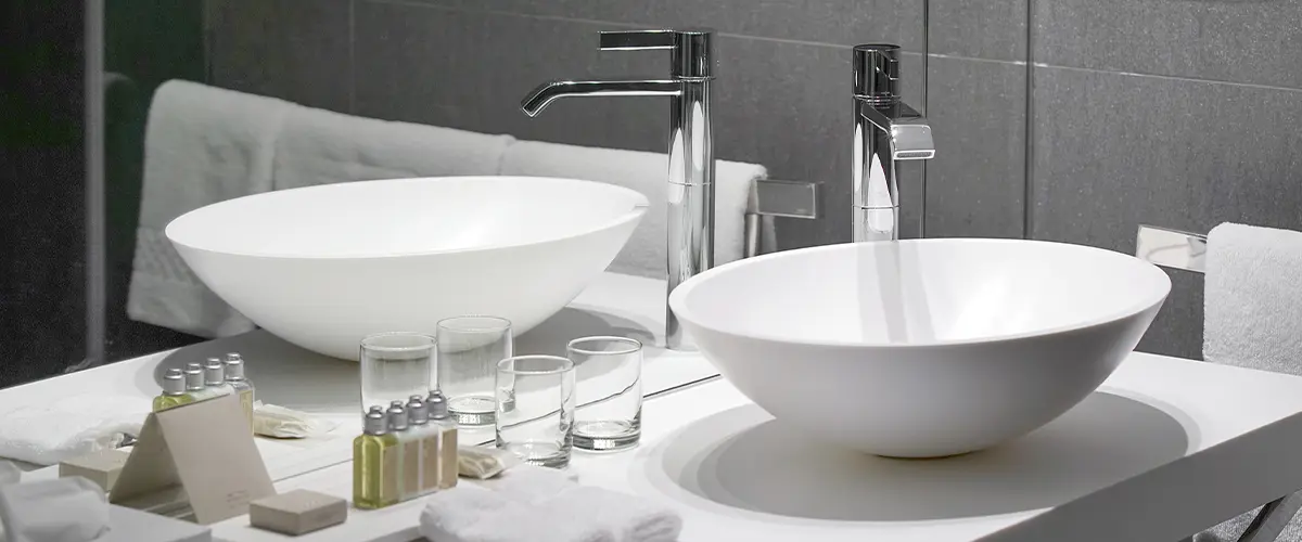 Modern bathroom with a white vessel sink, chrome faucet, and neatly arranged toiletries on a white countertop, reflected in a mirror