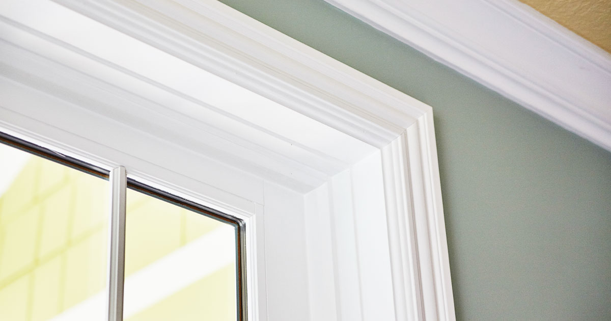 Close-up of a window frame with detailed white crown molding against a pale green wall