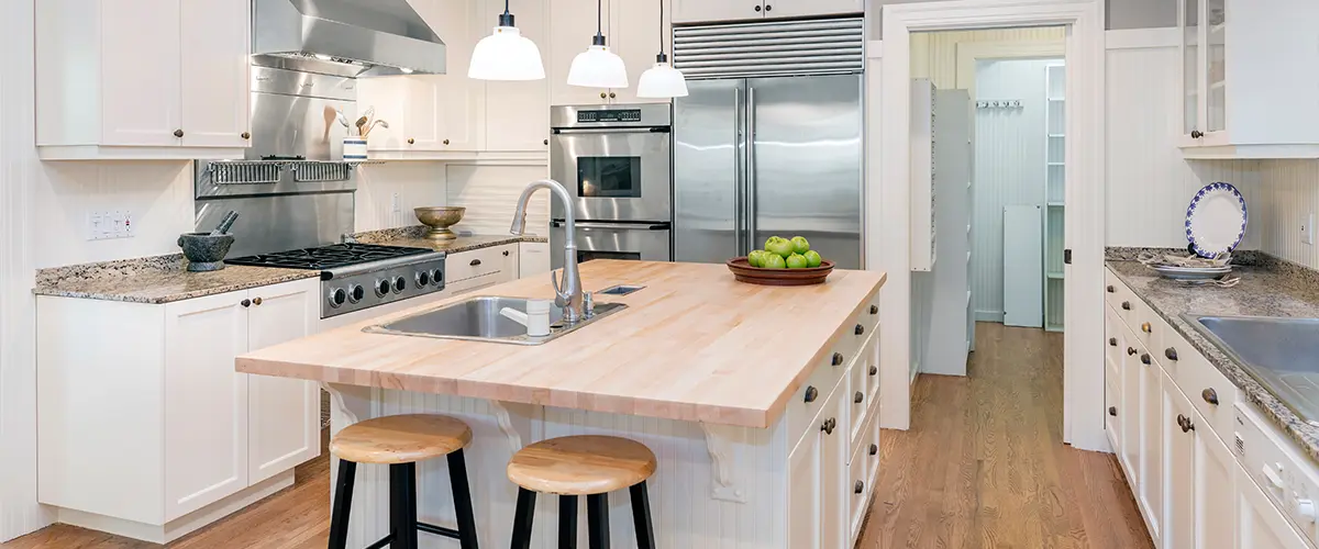 Modern white kitchen with butcher block island, stainless steel appliances, and pendant lighting.