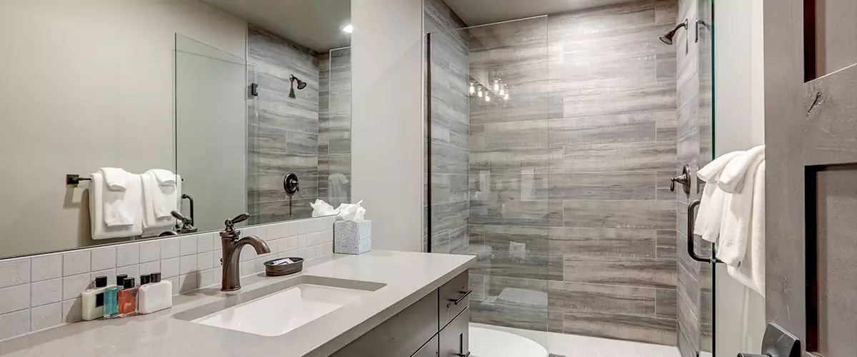 Natural new classic bathroom interior with new glass and ceramic tiles walk in shower and grey walls with white towels.