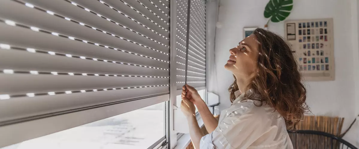 woman opening roller blind shutters on the balcony on a summer day