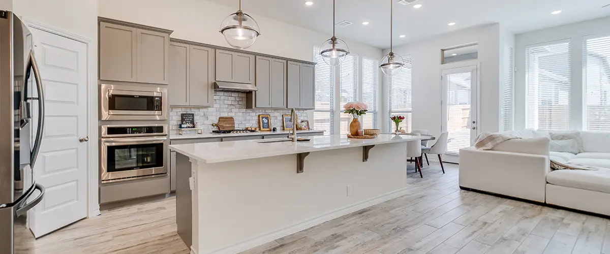 Bright open kitchen with gray cabinets, marble countertop, pendant lights, and adjoining living space - contemporary home interior.