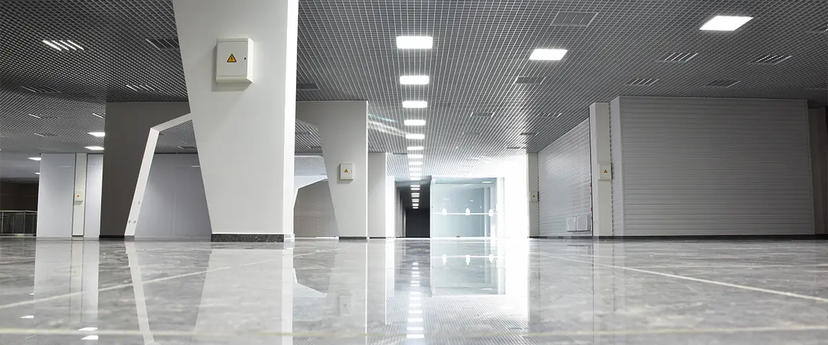 Empty commercial building interior with modern ceiling grid, reflective tile flooring, and fluorescent lighting - retail space for lease.