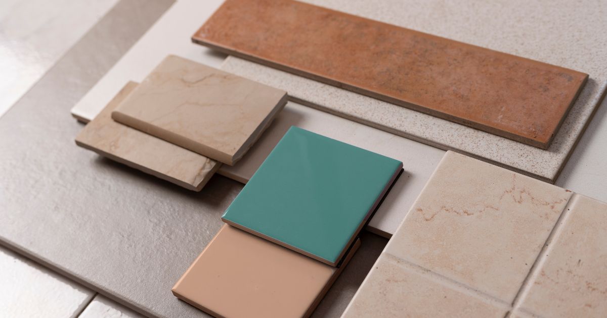 A collection of ceramic and porcelain tiles in various colors, finishes, and textures, including glossy green and beige tiles, matte stone-like tiles, and rustic terracotta pieces, arranged for design selection