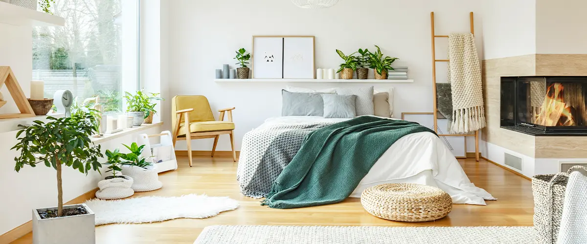 Cozy bedroom with modern decor, a fireplace, natural light, and indoor plants, creating a warm and inviting atmosphere.