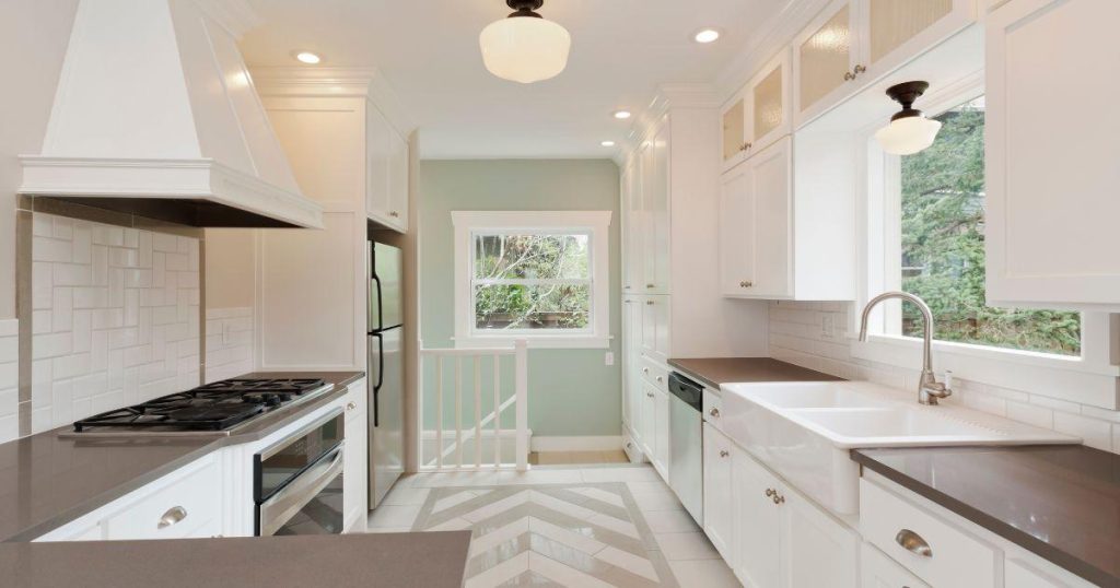 Bright white galley kitchen with chevron tile flooring and large window