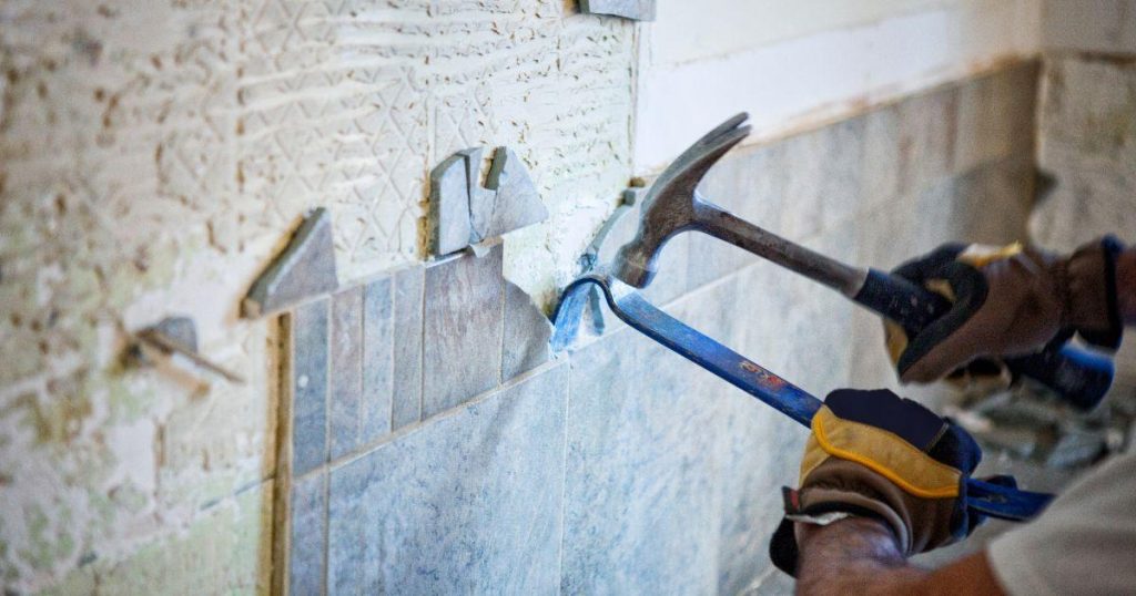 Worker removing old wall tiles with hammer and pry bar