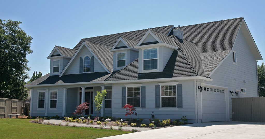 Large white house with dormer windows, grey roof shingles, and landscaped front yard.