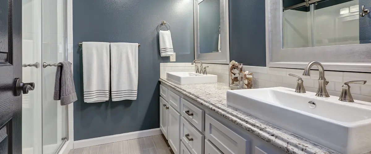 Modern bathroom with double vanity, vessel sinks, granite countertop, and dark blue accent wall.