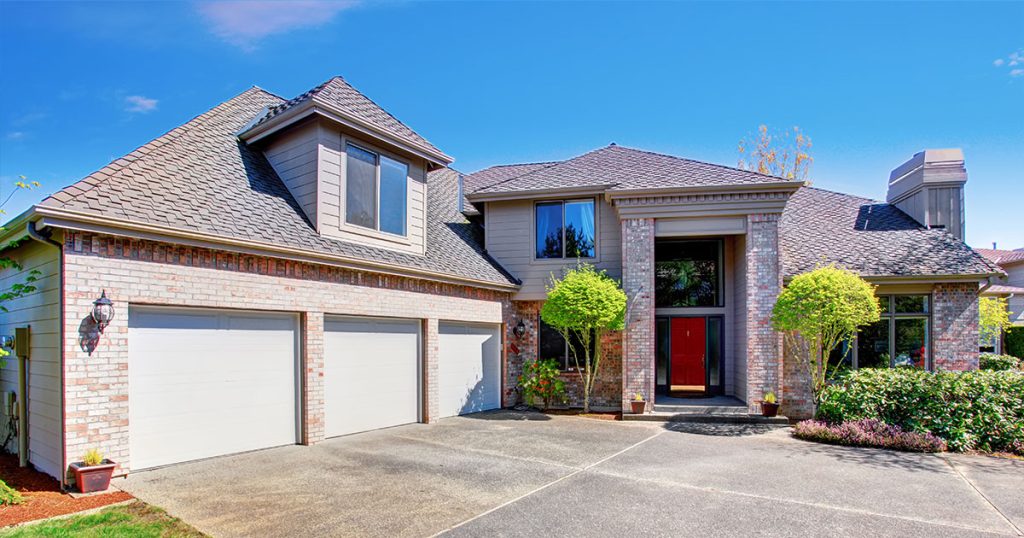 Modern brick home with three-car garage, landscaped front yard, and freshly poured concrete driveway.